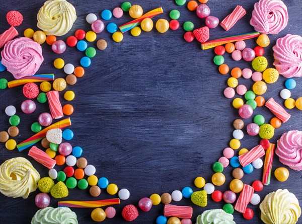 Colorful frame of multicolored candies on black wooden background. Circle copy space, top view, flat lay