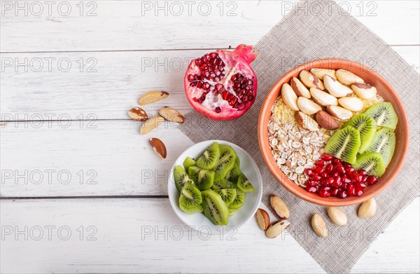 A plate with muesli, kiwi, pomegranate, Brazil nuts on a white wooden background. top view. copy space