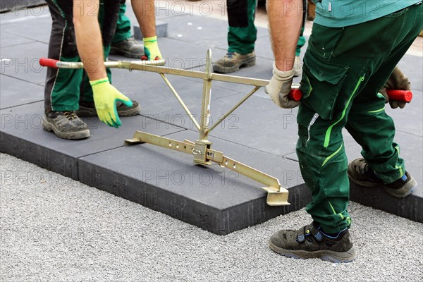 Workers lay heavy paving stones with a stone lifter