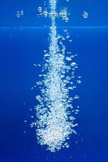 A thin jet of water penetrates the water surface and produces many air bubbles in the blue water of an aquarium