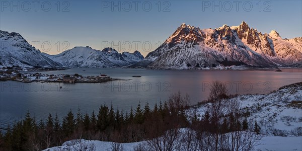 Die untergehende Sonne beleuchtet schneebedeckte Berge an einem ruhigen See, Lofoten