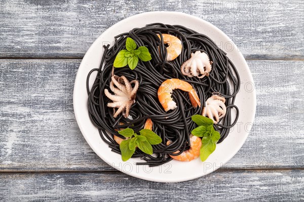 Black cuttlefish ink pasta with shrimps or prawns and small octopuses on gray wooden background. Top view, flat lay, close up
