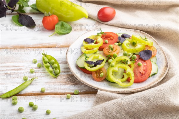 Vegetarian salad from green pea, tomatoes, pepper and basil on white wooden background and linen textile. Side view, close up