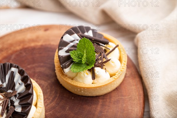 Sweet tartlets with chocolate and cheese cream with cup of coffee on a white wooden background and linen textile. side view, close up, selective focus