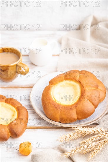 Sour cream bun with cup of coffee on a white wooden background and linen textile. Side view, close up, selective focus