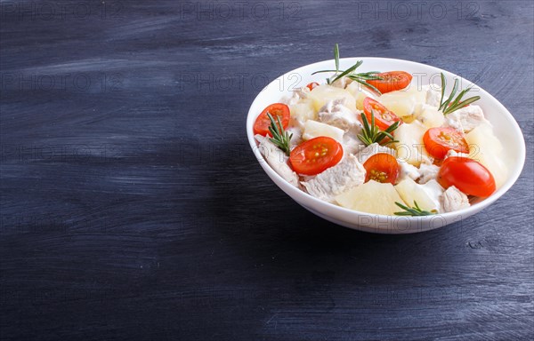 Chicken fillet salad with rosemary, pineapple and cherry tomatoes on dark blue wooden background. close up, copy space