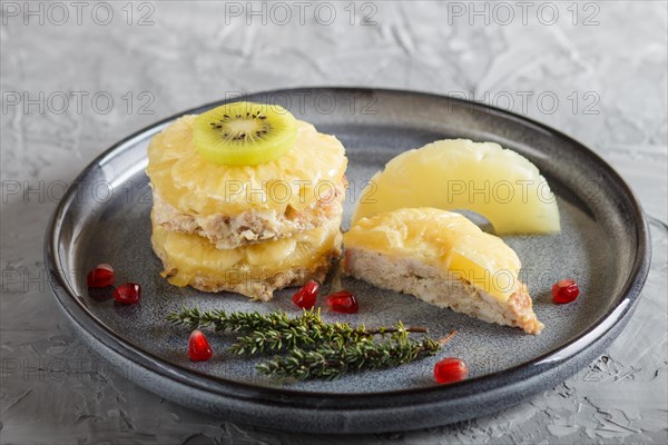 Pieces of baked pork with pineapple, cheese and kiwi on gray plate, side view, close up, selective focus