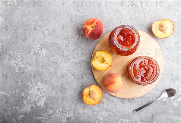 Peach jam in a glass jar with fresh fruits on gray concrete background. top view, flat lay, copy space