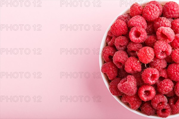 Fresh raspberry in white bowl on pink pastel background. top view, copy space, close up