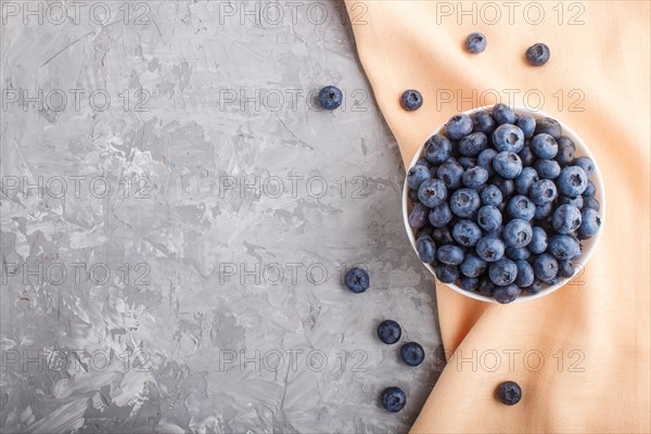 Fresh blueberry in white bowl and orange pastel textile on gray concrete background. top view, flat lay, copy space