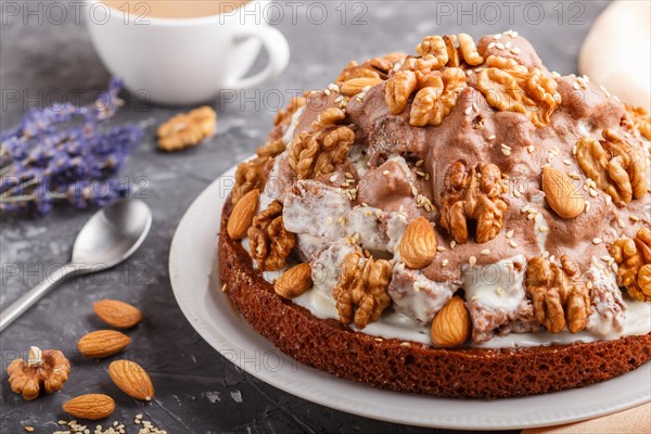 Homemade cake with milk cream, cocoa, almond, hazelnut on a black concrete background with orange textile and a cup of coffee. Side view, close up, selective focus