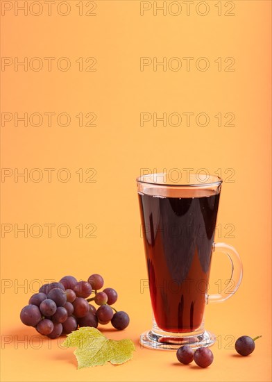 Glass of red grape juice on orange background. Morninig, spring, healthy drink concept. Side view, copy space