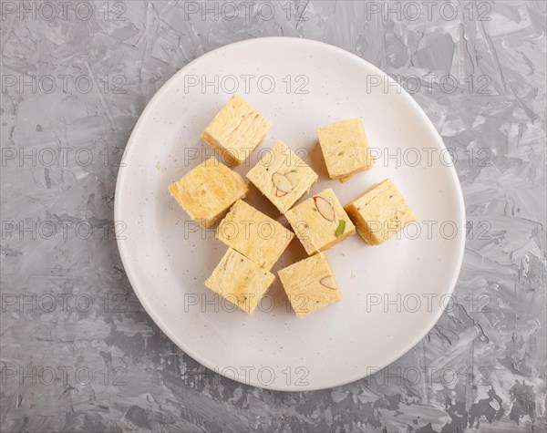 Traditional indian candy soan papdi in white plate with almond and pistache on a gray concrete background. top view, flat lay, close up