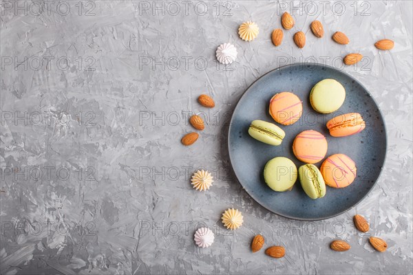 Orange and green macarons or macaroons cakes on blue ceramic plate on a gray concrete background. Flat lay, top view, copy space