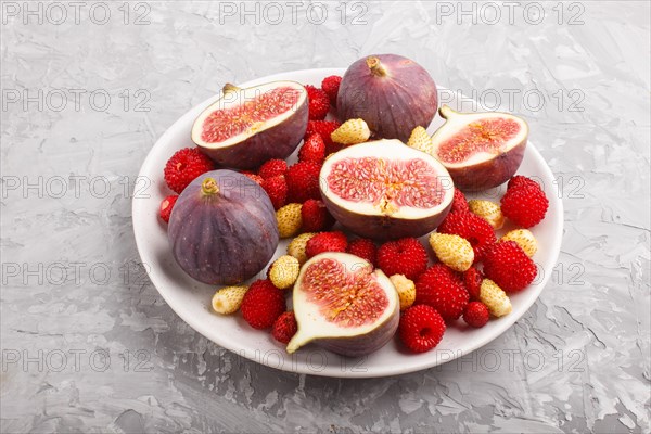 Fresh figs, strawberries and raspberries on white ceramic plate on gray concrete background. side view, close up