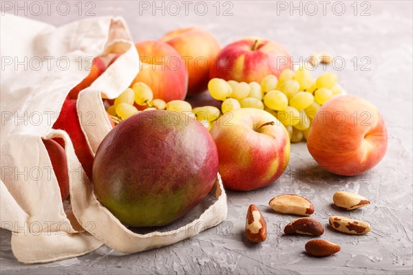 Fruits in reusable cotton textile white bag. Zero waste shopping, storage and recycling concept, eco friendly lifestyle. Side view, close up. Peach, apple, nuts, mango, grape