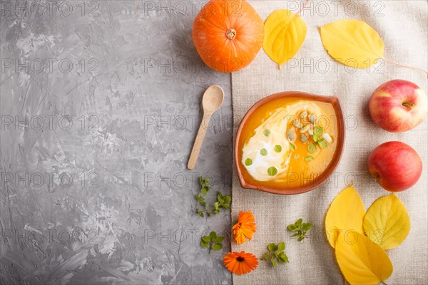 Traditional pumpkin cream soup with seeds in clay bowl on a gray concrete background with linen textile. top view, flat lay, copy space
