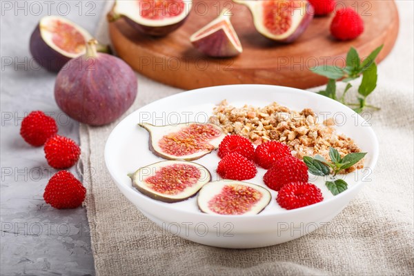 Yoghurt with raspberry, granola and figs in white plate on a gray concrete background and linen textile. side view, close up, selective focus
