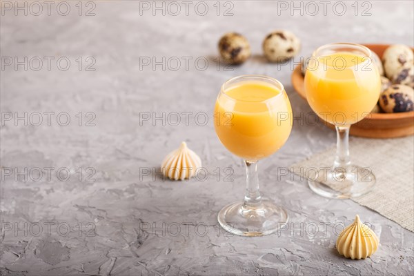 Sweet egg liqueur in glass with quail eggs and meringues on a gray concrete background. Side view, copy space