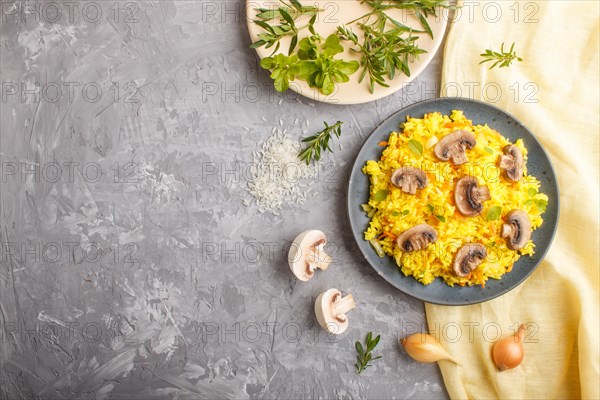 Yellow fried rice with champignons mushrooms, turmeric and oregano on blue ceramic plate on a gray concrete background and yellow textile. Top view, flat lay, copy space