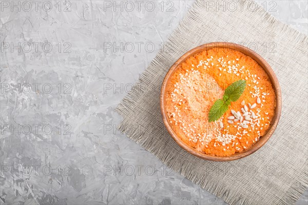 Carrot cream soup with sesame seeds in wooden bowl on a gray concrete background with linen textile. top view, flat lay, copy space