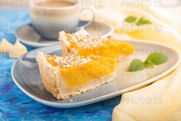Two pieces of traditional american pumpkin pie with cup of coffee on a blue concrete background and yellow textile. side view, close up, contrast, selective focus