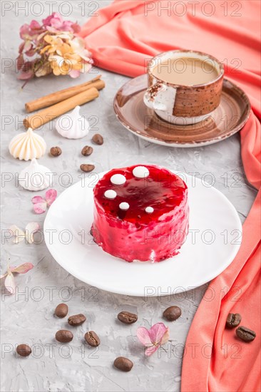 Red cake with souffle cream with cup of coffee on a gray concrete background and red textile. side view, close up