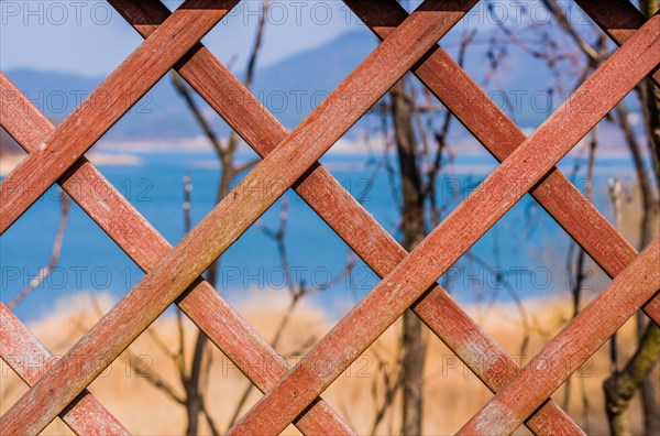 Selective blurring of lake and trees seen through in focus lattice work of fence in South Korea