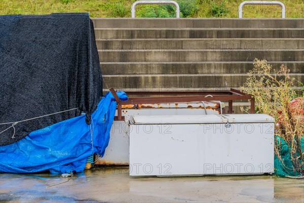 Old abandoned refrigerator laying on wet concrete in front of stairway on rainy morning in South Korea