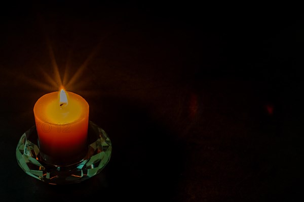 Burning candle in glass holder isolated on black textured background. Small amount of grain added for effect