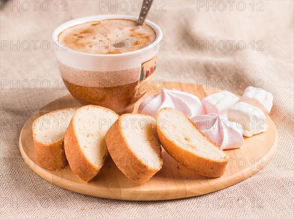 Sweet buns, meringues and coffee cup on a wooden board and linen tablecloth