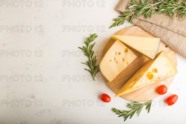 Various types of cheese with rosemary and tomatoes on wooden board on a white wooden background and linen textile. Top view, close up, copy space, flat lay