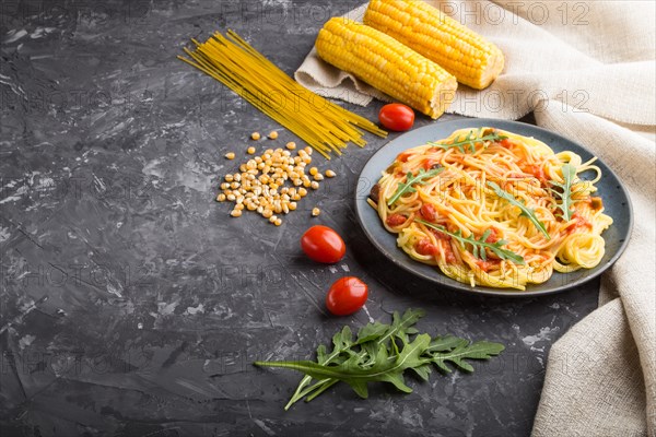 Corn noodles with tomato sauce and arugula on a black concrete background and linen textile. Side view, copy space