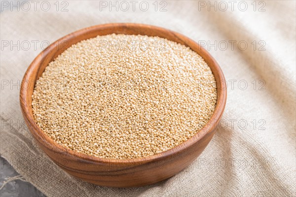 Wooden bowl with raw white quinoa seeds and wooden spoon on a gray concrete background and linen textile. Side view, close up, selective focus