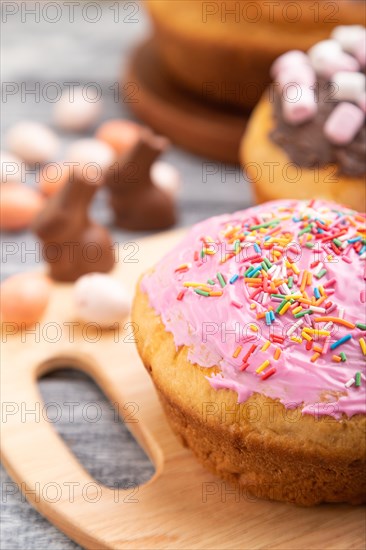 Homemade glazed and decorated easter pies with chocolate eggs and rabbits on a gray wooden background and linen textile. Side view, selective focus, close up