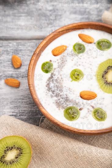 Yogurt with kiwi, gooseberry, chia and almonds in wooden bowl on gray wooden background and linen textile. Side view, close up, selective focus