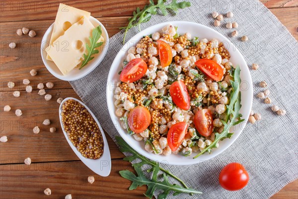 Vegetarian salad of boiled chickpeas, cheese, arugula, mustard and cherry tomatoes on brown wooden background. close up, top view