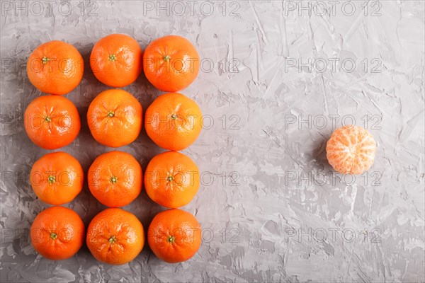 Rows of tangerines forming a rectangle and one peeled tangerine on a gray concrete background, top view, flat lay