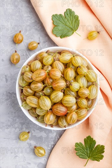 Fresh green gooseberry in white bowl with orange textile on gray concrete background. top view, close up, flat lay