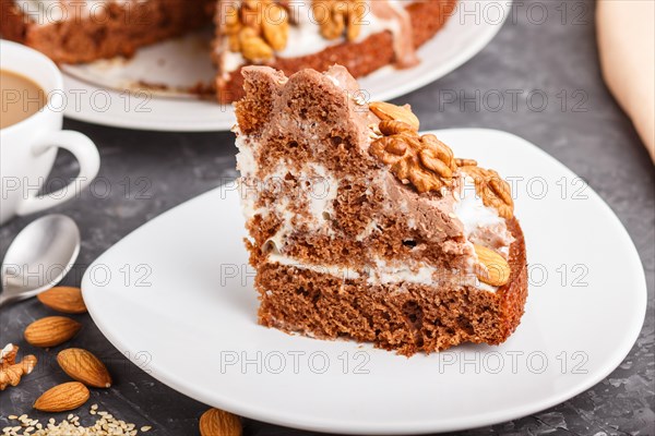 Homemade cake with milk cream, cocoa, almond, hazelnut on a black concrete background and a cup of coffee. Side view, close up, selective focus