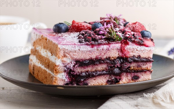 Berry cake with milk cream and blueberry jam on blue ceramic plate with cup of coffee and fresh blueberries on a white wooden background. side view, close up, selective focus