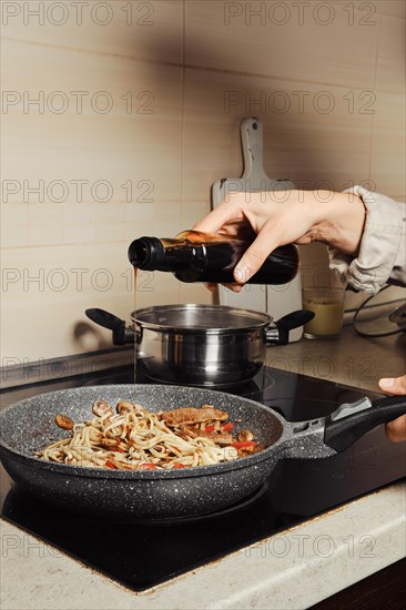 Unrecognizable woman pouring oyster sauce into noodles in a frying pan