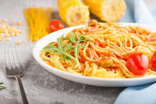 Corn noodles with tomato sauce and arugula on a gray concrete background and blue textile. Side view, close up, selective focus