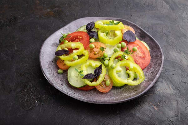 Vegetarian salad from green pea, tomatoes, pepper and basil on a black concrete background. Side view, close up