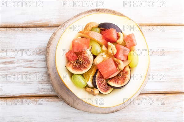 Vegetarian fruit salad of watermelon, grapes, figs, pear, orange, cashew on white wooden background. Top view, flat lay, close up