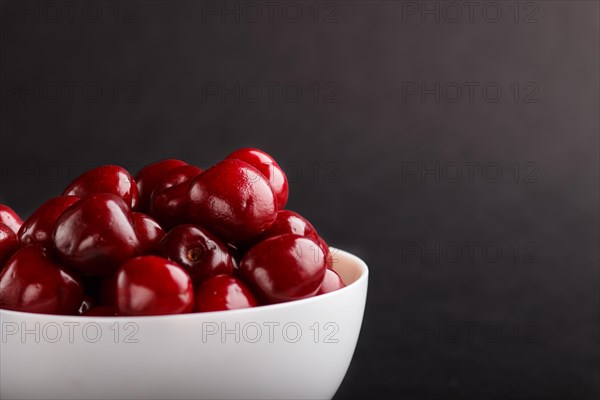 Fresh red sweet cherry in white bowl on black background. side view, copy space, close up