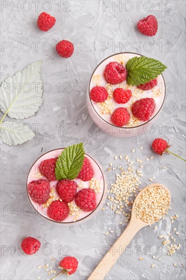 Yoghurt with raspberry and sesame in a glass and wooden spoon on gray concrete background. top view, flat lay, close up