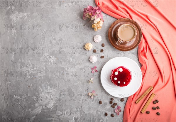 Red cake with souffle cream with cup of coffee on a gray concrete background and red textile. top view, flat lay, copy space