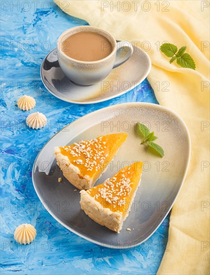 Two pieces of traditional american pumpkin pie with cup of coffee on a blue concrete background and yellow textile. side view, close up, contrast