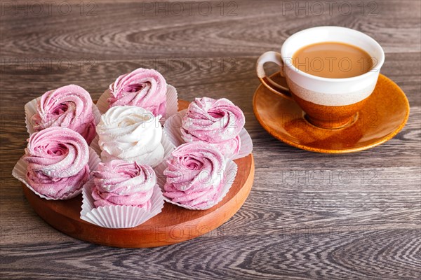 Pink and white marshmallows (zephyr) on a round wooden board with cup of coffee on a gray wooden background